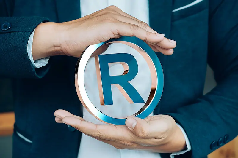 Imagem de um homem segurando o símbolo de registro de marca. Assessoria para registro de marca que inclui desde o pedido de registro da marca até a análise do INPI (decisão final da possibilidade de registro de marca). Caso a marca seja aceita, realizamos a concessão do registro da marca.